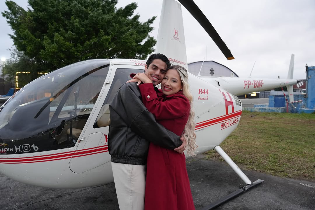 Casal abraçado ao lado de um helicóptero no Campo de Marte